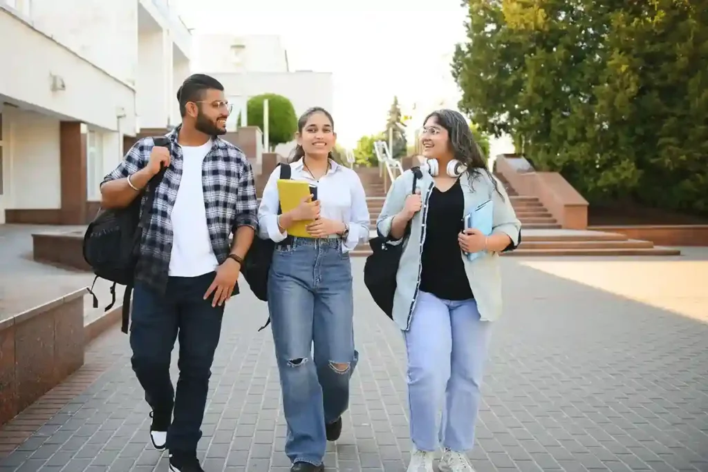 Three smiling college students walking together outdoors on campus with backpacks and books.